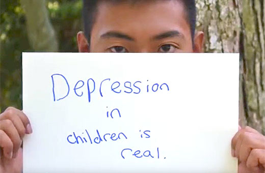 Photo of a young person holding a white paper hand-written sign that says Depression in Children is Real